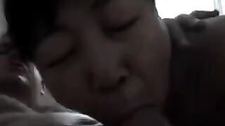 A Chinese woman practices her sucking dick skills on a guy in bed